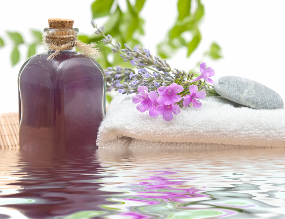 Frasco de aceite aromático con flores, toalla y piedras